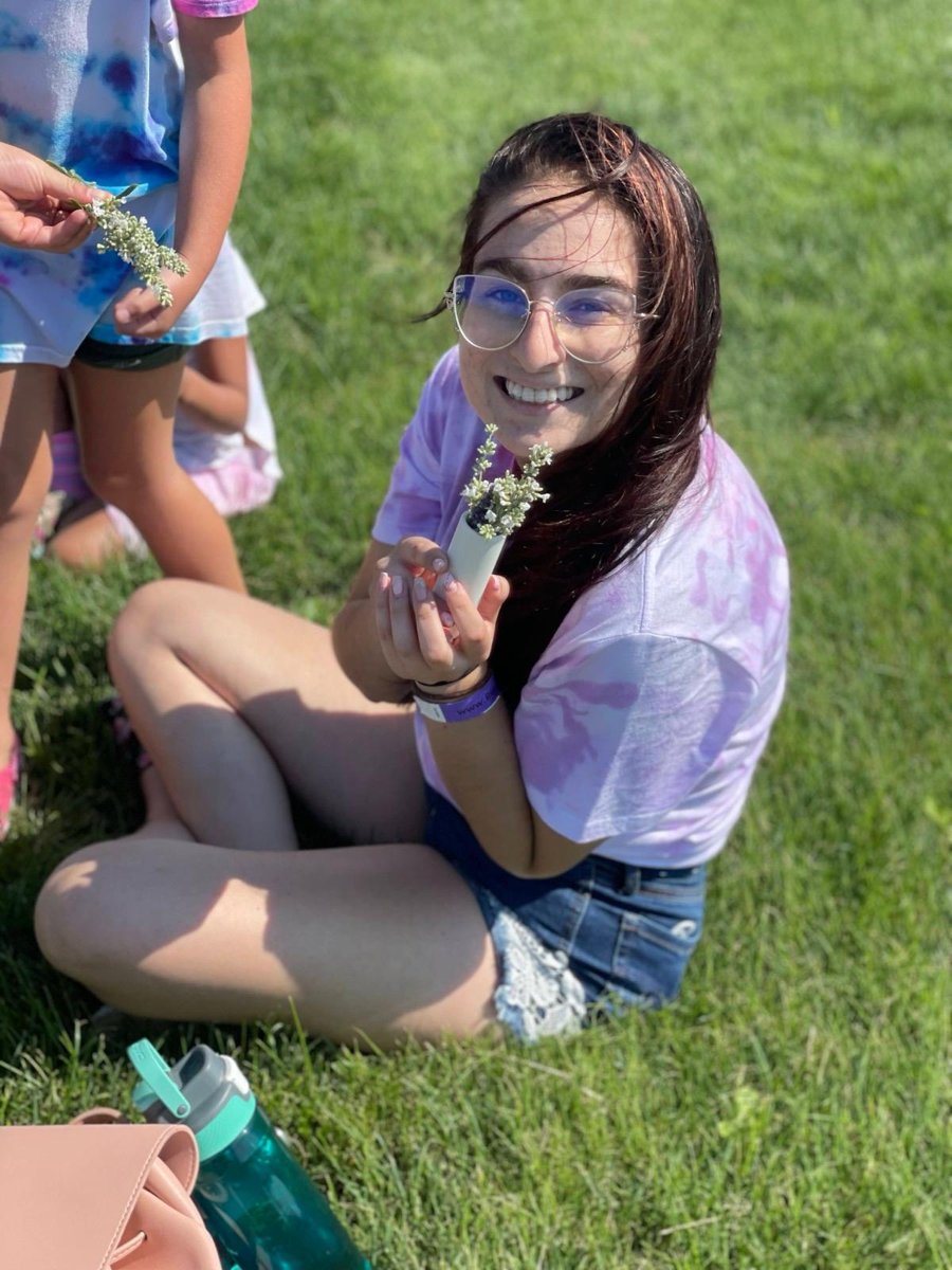 Ms. Ally smiling while sitting on the grass holding a small bouquet of wildflowers