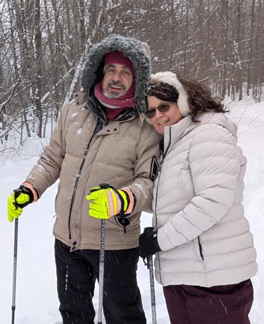 Frank and Royanne Naccarato smiling together while snowshoeing on a snowy forest trail