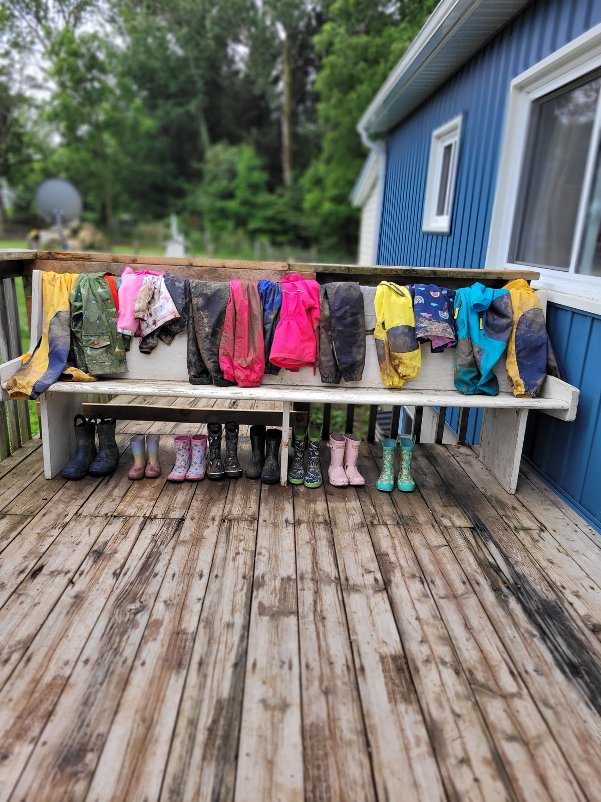 Muddy rain suits and rubber boots lined up on a deck after a day outdoors