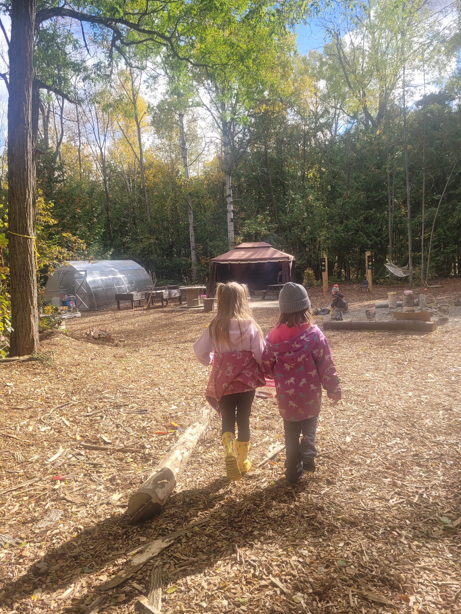 Two children walking hand in hand across the woodchip forest school campus